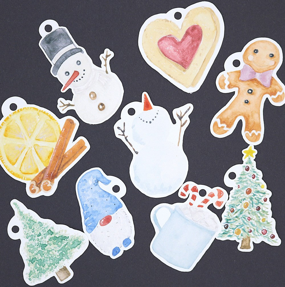 Detailfoto aus dem Xmas Special Set mit weihnachtlichen Aquarell-Anhängern für Geschenke; wie Schneemännern, Herz, Lebkuchenfigur, Zimt-Orangen-Motiv, Weihnachtsbaum, Wintermütze und Kakao, dekorativ auf dunklem Hintergrund ausgelegt.