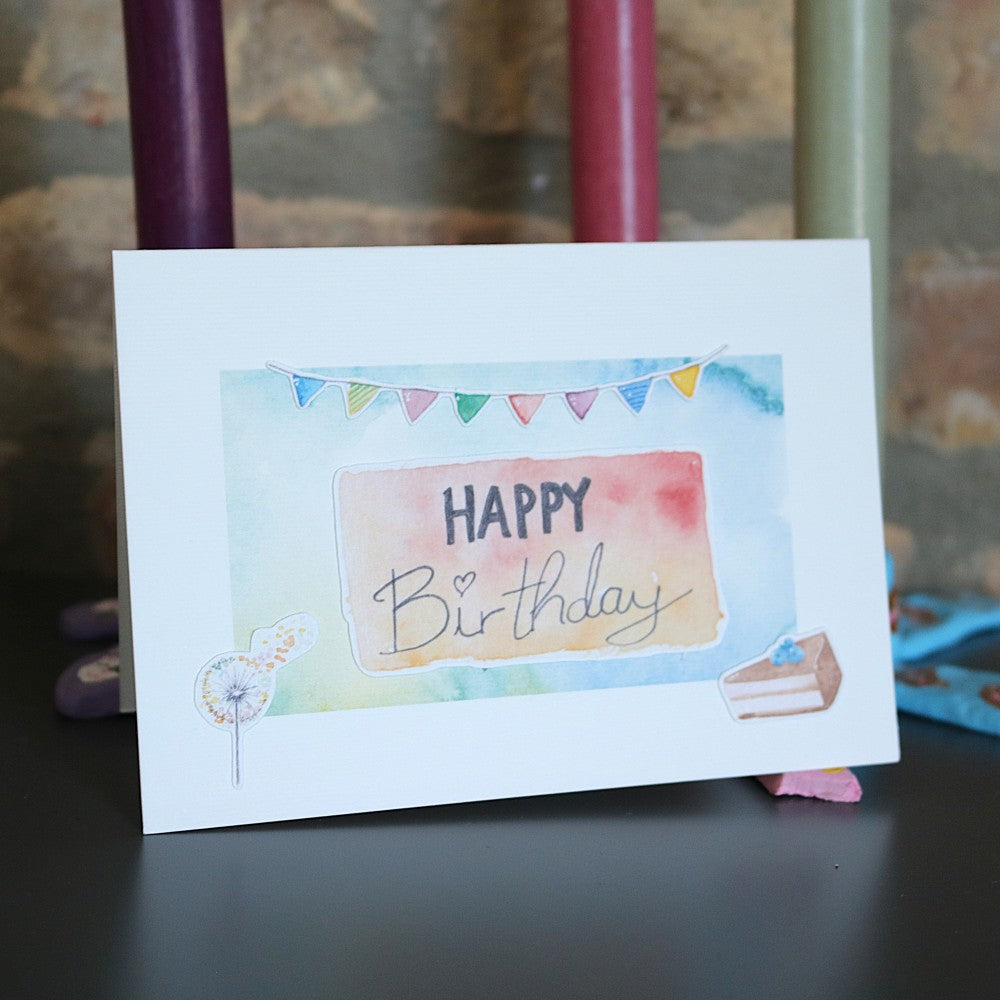Geburtstagskarte mit zartem Aquarellhintergrund, „Happy Birthday“-Schriftzug, bunter Wimpelkette und kleinen Kuchen-Illustrationen als 3D-Elemente.