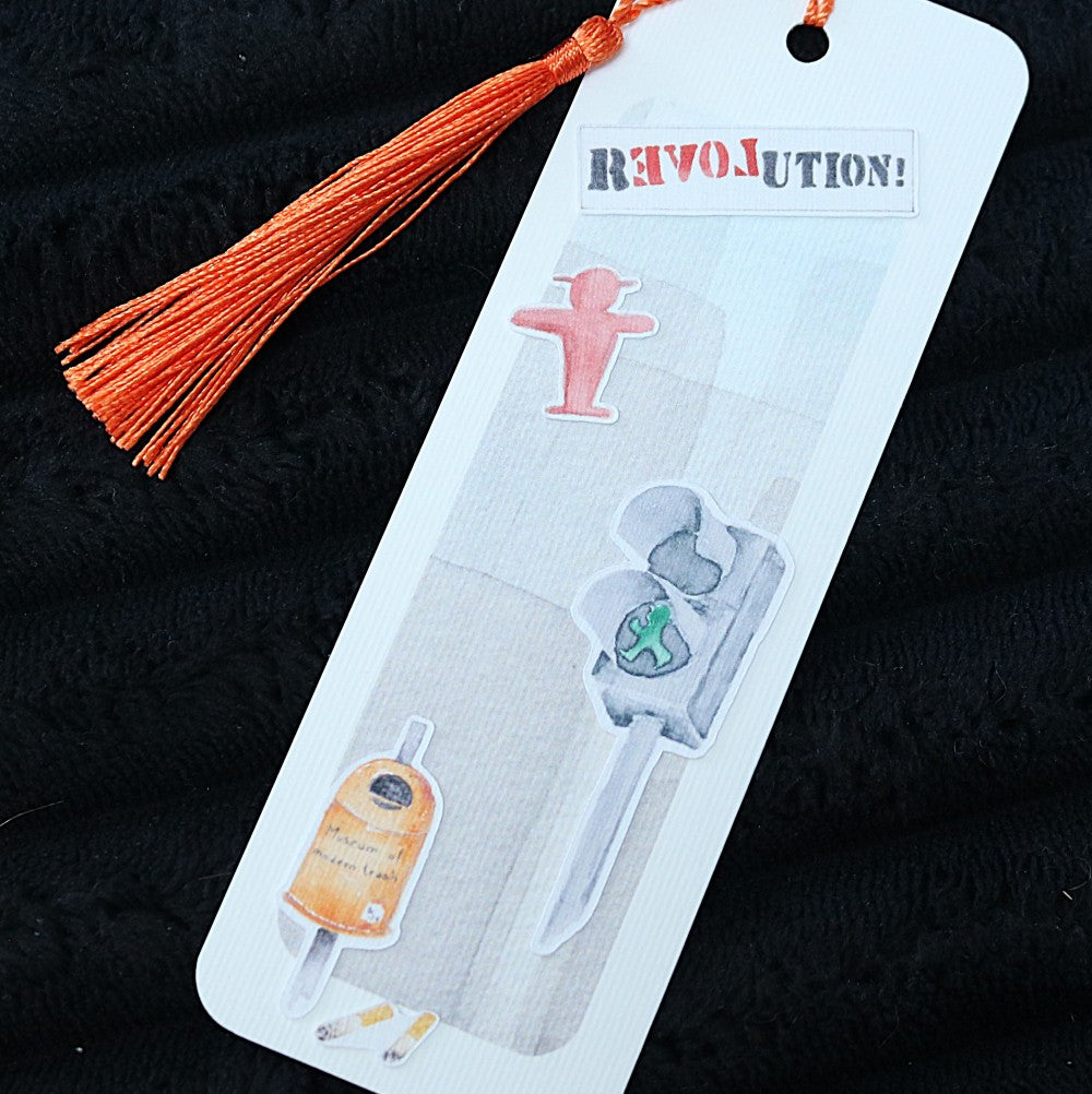 Berlin-Lesezeichen mit Aquarellmotiven wie Ampelmännchen, Berliner Bär, Mülleimer und Schriftzug „Revolution“, mit orangefarbener Quaste.
