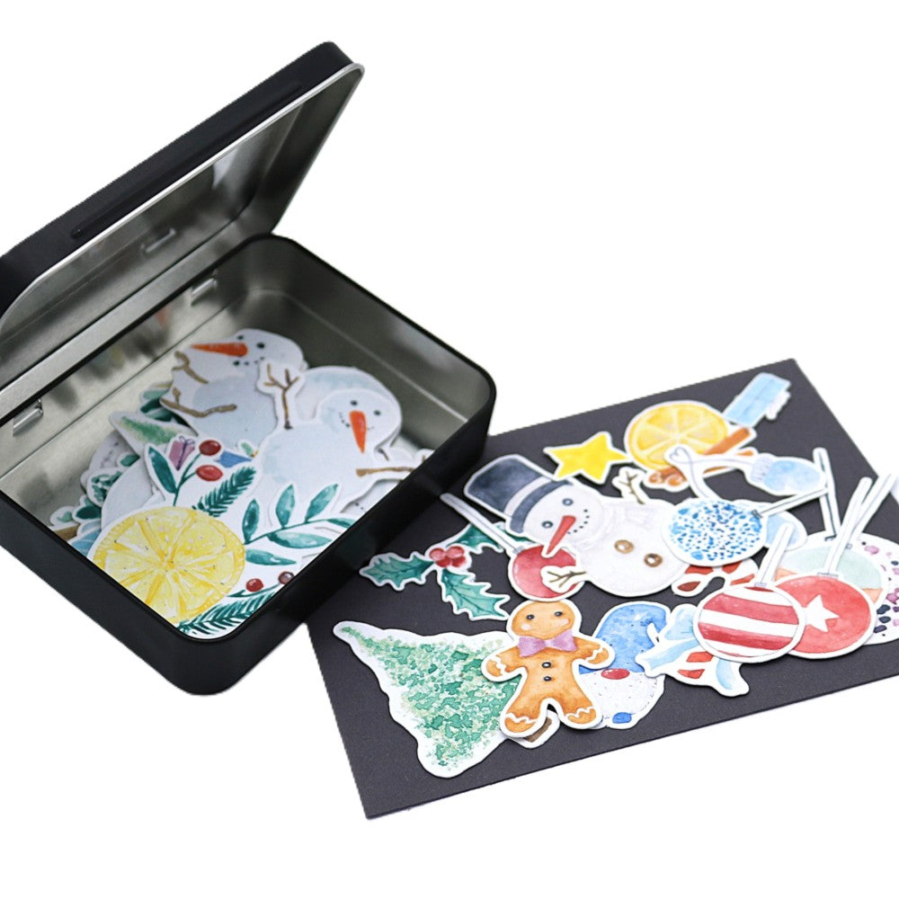 Geöffnete schwarze Stickerbox der Weihnachts-Edition, gefüllt mit winterlichen Aquarell-Stickern wie Schneemännern, Wichteln, Lebkuchenfigur, Tannenbaum und weiteren festlichen Motiven; einige Sticker liegen dekorativ vor der Box auf dunklem Untergrund.