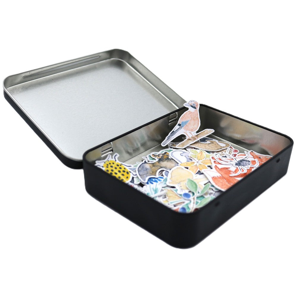 Geöffnete schwarze Metallbox der Waldbewohner Deluxe Edition mit bunt gemischten Aquarell-Stickern im Inneren; ein Vogelmotiv steht leicht herausragend über den restlichen Stickern.