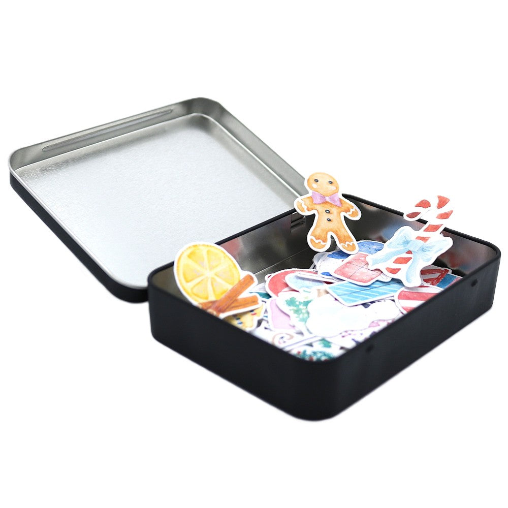 Geöffnete schwarze Metallbox der Deluxe-Weihnachtsedition, gefüllt mit farbenfrohen Aquarell-Stickern wie Lebkuchenfigur, Zuckerstange, Zimtstangen und weiteren winterlichen Motiven; der Deckel liegt nach hinten aufgeklappt.