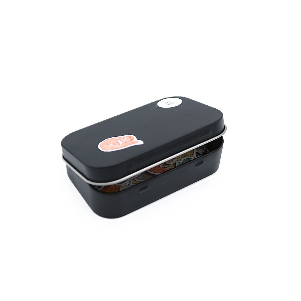 Geschlossene schwarze Metallbox der Waldbewohner Classic Edition mit sichtbaren Aquarell-Stickern im Inneren; auf dem Deckel befindet sich ein kleines Fuchs-Motiv.