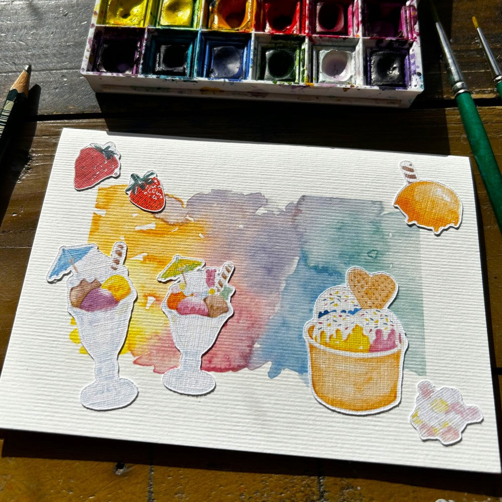 Karte mit Eismotiven auf einem Tisch mit Aquarell Farbkasten, Pinsel und Bleistift