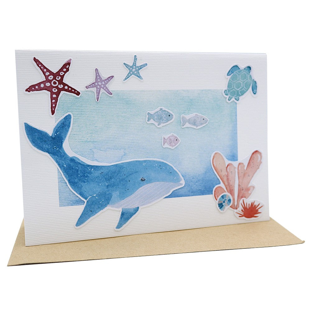 Klappkarte mit Wal, Fischen, Seesternen und Korallen, darunter ein Kraftpapier Umschlag