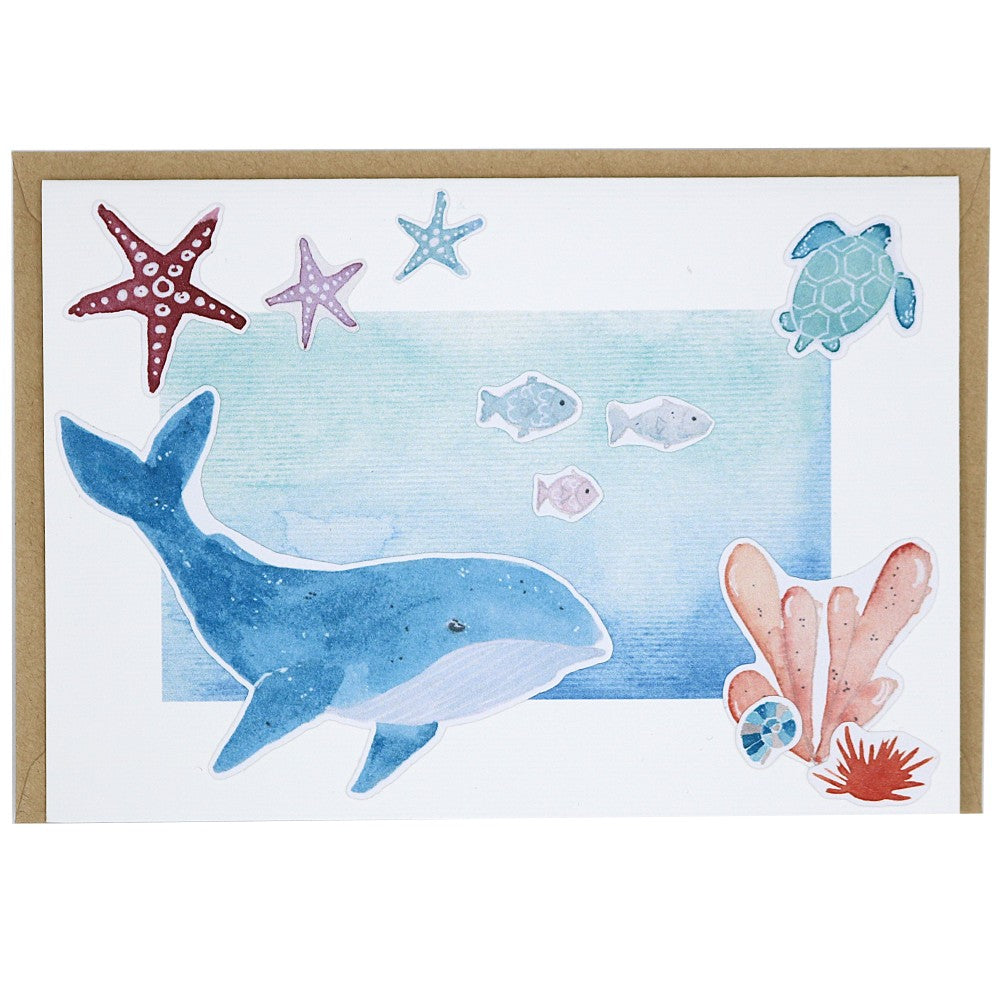 Grusskarte mit großem Wal und Fischen, Seesternen und Schildkröte, dahinter ein Kraftpapier Umschlag 