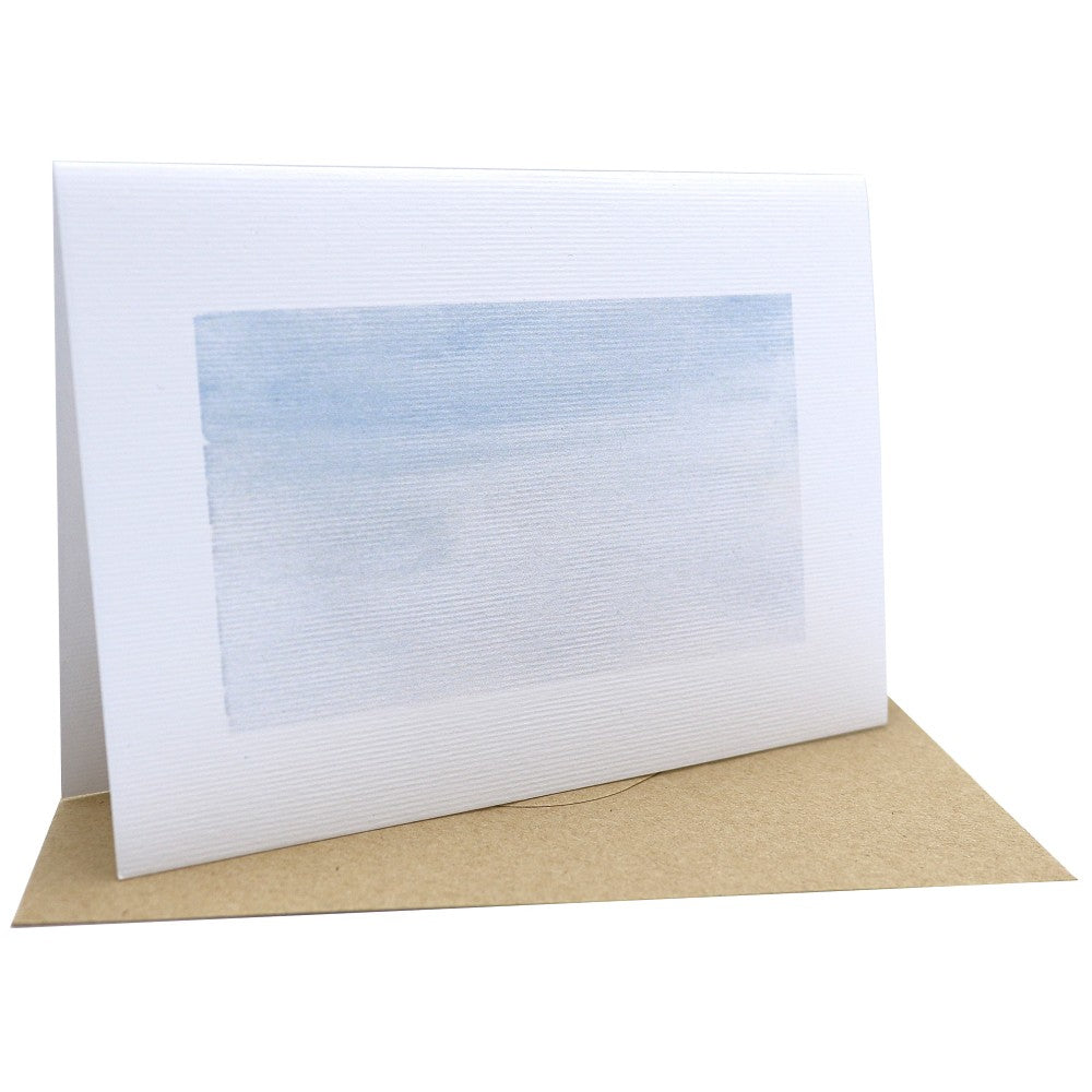Klappkarte aus Aquarellpapier mit winterlichem Aquarellhintergrund in zarten Blau- und Weißtönen; im Vordergrund liegt ein Kraftpapier-Umschlag auf weißem Hintergrund.