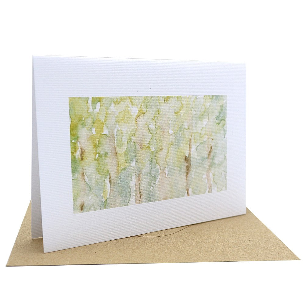 Klappkarte „Waldbewohner“ mit Aquarellmotiv in warmen Grün- und Naturtönen – eine lichte Baumgruppe im Wald, zart und lebendig illustriert; gedruckt auf strukturiertem Aquarellpapier, kombiniert mit braunem Kraftpapier-Umschlag; aufgestellt dargestellt.