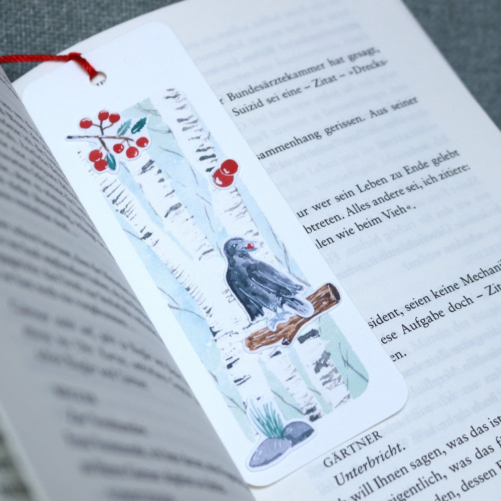 Lesezeichen Waldbewohner: Aquarell-Lesezeichen mit Birkenstämmen, roten Beeren, einem Raben auf einem Ast und kleinen Waldboden-Details; rotes Bändchen als Quaste