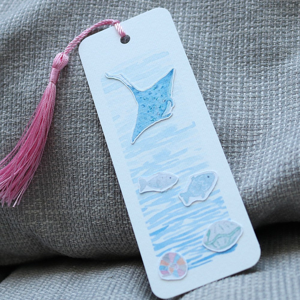 Lesezeichen Im Meer: Aquarell-Lesezeichen mit blauem Rochen, Fischen und Muschelmotiven auf blauem Hintergrund, mit rosafarbener Quaste