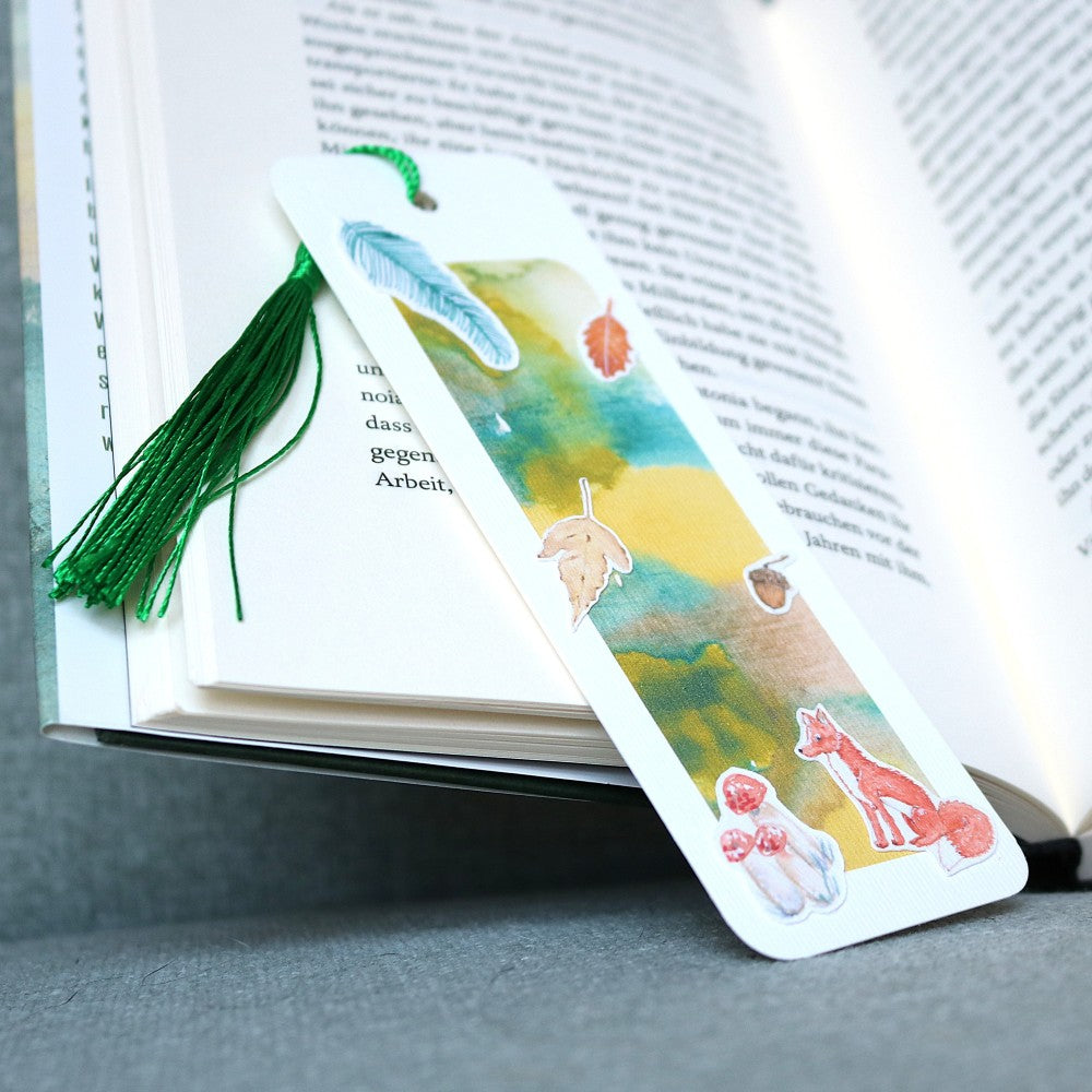 Lesezeichen Waldbewohner: Aquarell-Lesezeichen in Grün-Gelb-Tönen mit Fuchs, Pilzen, Blatt und Eichel, mit dunkelgrüner Quaste
