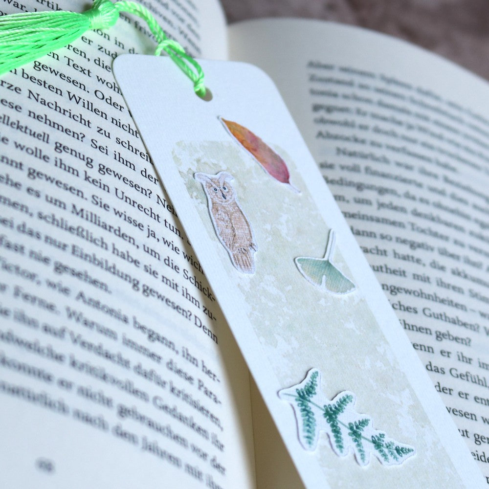 Lesezeichen Waldbewohner: Aquarell-Lesezeichen mit hellgrünem Waldhintergrund und Motiven wie Eule, Blättern und Farn, mit grüner Quaste