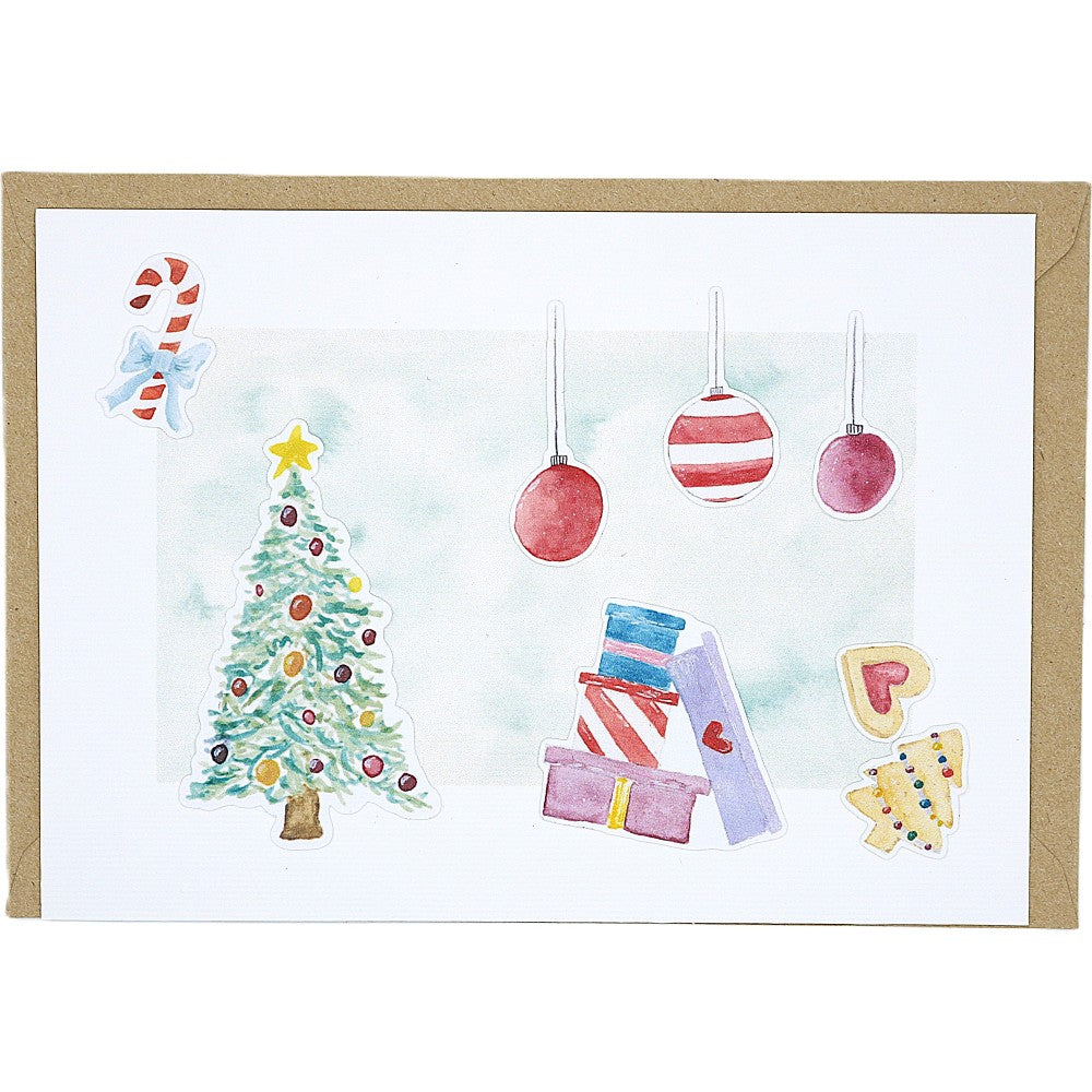 Weihnachtliche Postkarte auf strukturiertem Aquarellpapier, beklebt mit Mini-Aquarellmotiven: geschmückter Weihnachtsbaum, Zuckerstange, hängende Weihnachtskugeln, Geschenkstapel und kleine Plätzchen; dahinter ein liegender Kraftpapierumschlag.