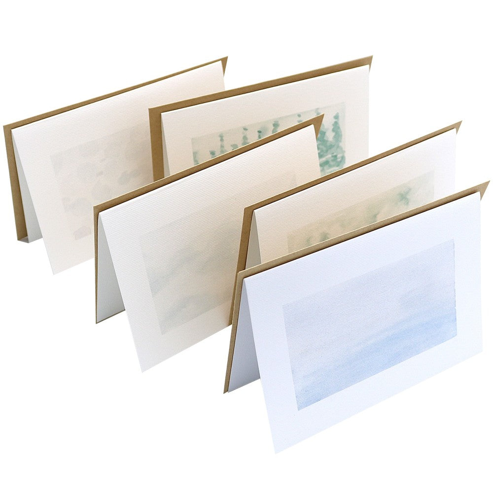 Mehrere weihnachtliche Klappkarten aus Aquarellpapier in einer Reihe auf weißem Hintergrund; jede Karte mit einem zarten, winterlichen Aquarell-Hintergrund in Grün- und Blautönen; dazu passende Kraftpapier-Umschläge.