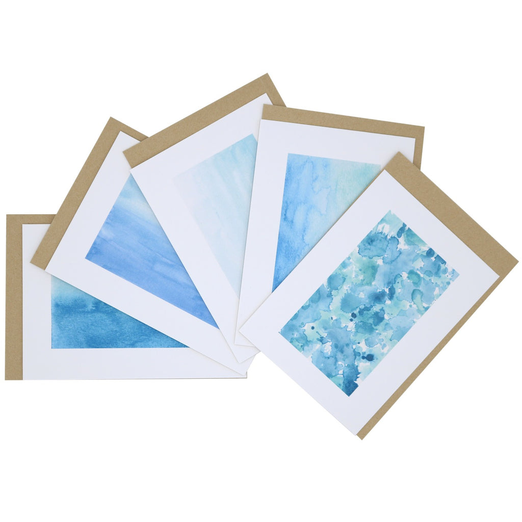 „Fächerförmig ausgebreitetes Postkarten-Set Im Meer mit fünf Aquarellmotiven in Blau- und Türkistönen, inspiriert von Wasser, Wellen und Küste, inklusive Kraftpapierumschlägen.“