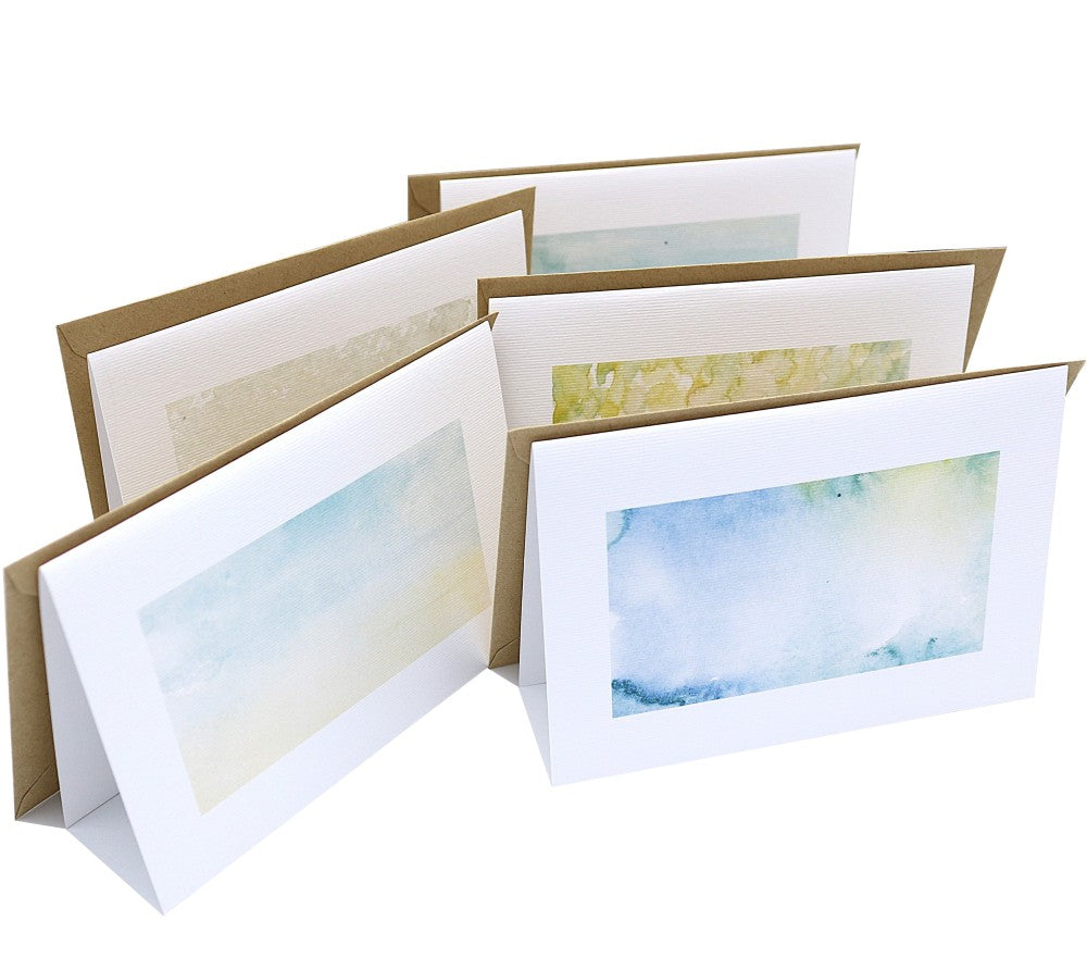 Aufgestelltes Waldbewohner Klappkarten Set aus mehreren Klappkarten mit unterschiedlichen Aquarellhintergründen in sanften Natur- und Grüntönen. Die Karten bestehen aus strukturiertem Aquarellpapier und stehen leicht versetzt nebeneinander. Dahinter liegen passende Kraftpapier-Umschläge. Das Set gehört zur Waldbewohner-Kollektion und zeigt die Hintergründe ohne Motive.