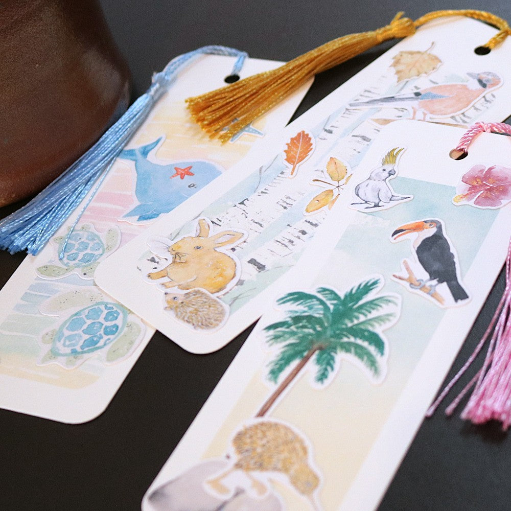 Drei Lesezeichen mit Tiermotiven aus Aquarell auf Aquarellhintergründen; nebeneinander überlagernd liegend; mit Lesezeichenbändchen und Quaste. 