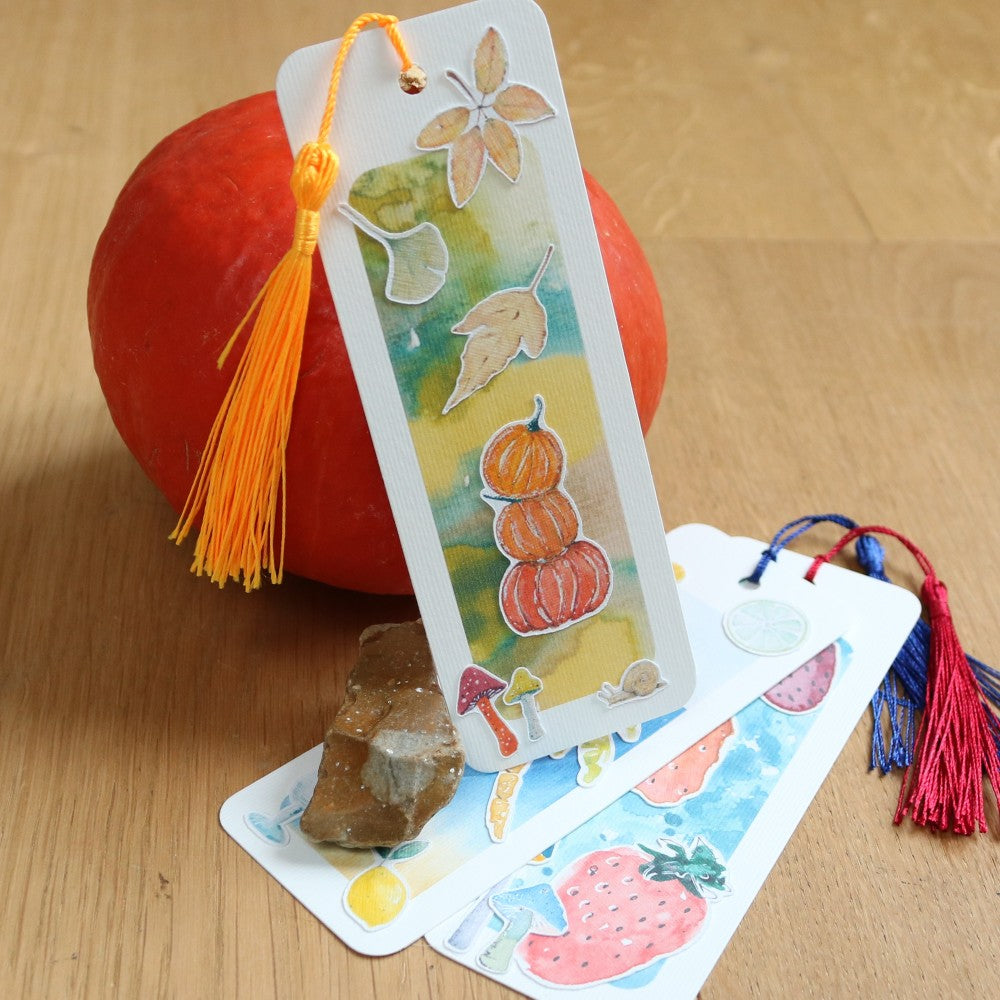 Drei Lesezeichen, eines aufgestellt mit Kürbissen und Blätter, die anderen beiden darunter liegend; mit Quasten Lesezeichenbändchen